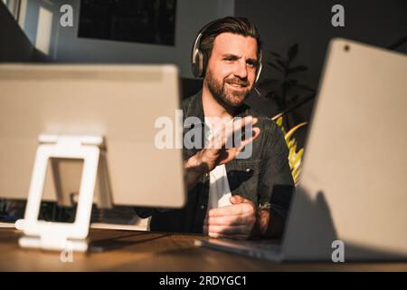 Happy freelancer wearing headset gesturing and talking on video call Stock Photo