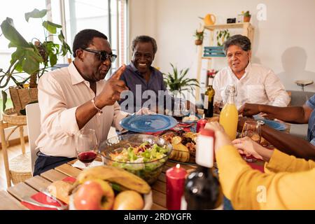 Senior man talking with friends with food on dining table at home Stock Photo