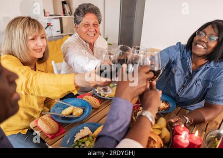 Happy senior multiracial friends toasting wineglasses at dinner party Stock Photo