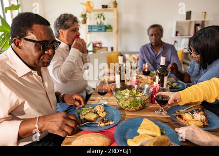 Senior friends enjoying food and drinks sitting at dining table Stock Photo