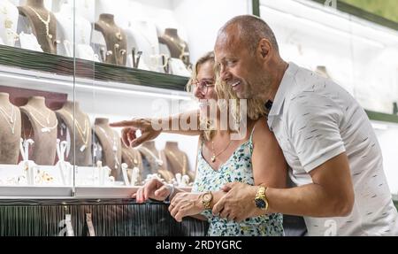 Middle-aged couple in love looking at gold and silver rings or chains in jewelry store. Stock Photo