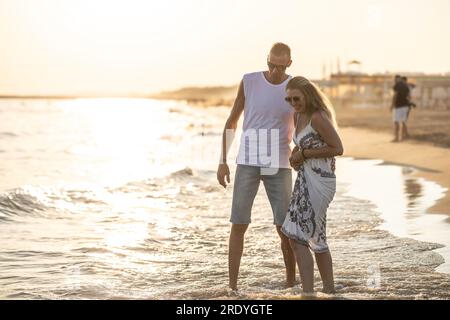 Happy middle-aged couple in love walking in the water on the beach at sunset. Stock Photo