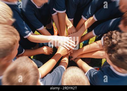 Many Happy Children Stacking Their Hands In A Teamwork Effort Before Playing Sports Game. Junior Football Team Stacking Hands Before a Match Stock Photo