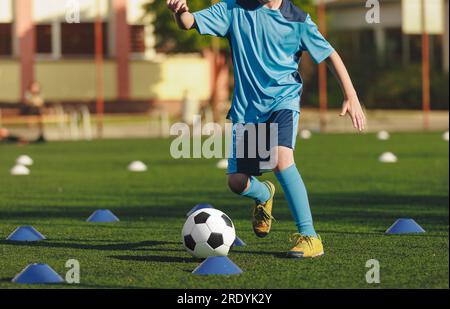 Physical education training class for children. Kids kicking classic soccer ball on slalom drill. Legs of school boy running fast and kicking soccer b Stock Photo