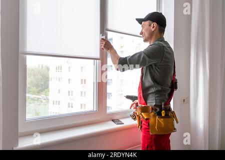 Worker in uniform installing blinds on plastic upvc window. Stock Photo