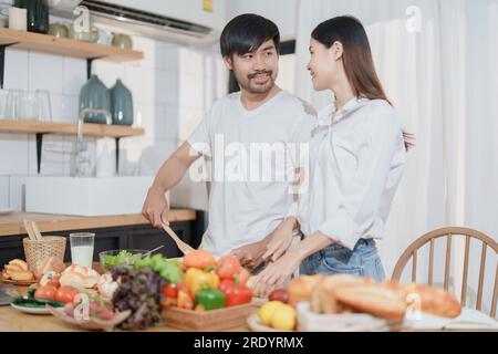 Smiling man hugging woman, two people standing and joyfully looking at each other. Young couple happily spending time in cozy modern kitchen at home. Stock Photo