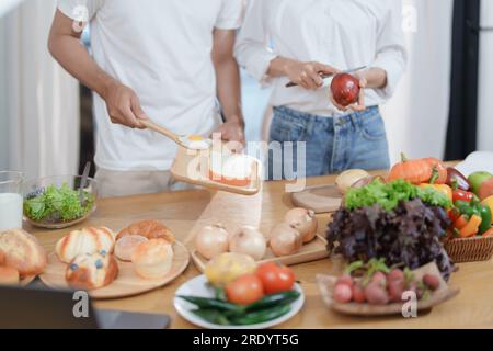 Smiling man hugging woman, two people standing and joyfully looking at each other. Young couple happily spending time in cozy modern kitchen at home. Stock Photo