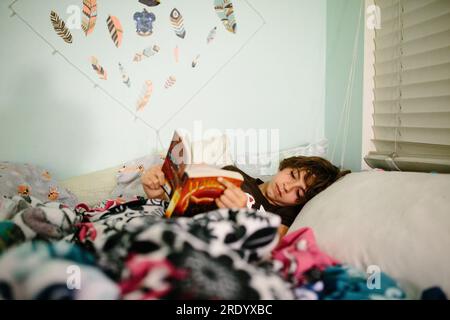 Teen girl lies in bed reading a book before bedtime Stock Photo