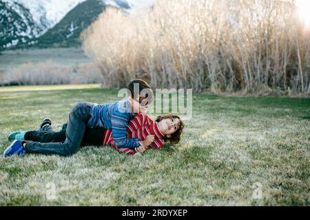 Little brother pins teen sister on the grass as they wrestle Stock Photo