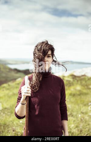 hiking girl smiles with wind blowing hair on wild coastline Stock Photo
