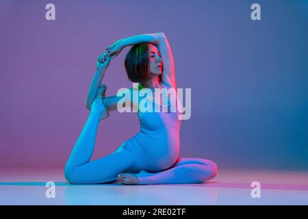 Pregnant woman doing legs stretching yoga exercises in neon Stock Photo