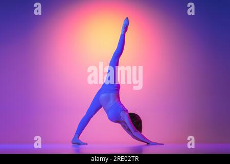 Pregnant woman doing one legged dog pose exercise in neon Stock Photo