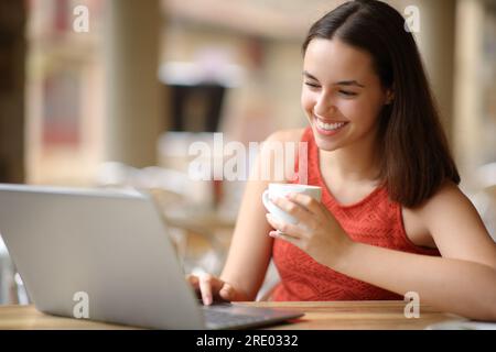 Happy woman is using a laptop sitting in a coffee shop Stock Photo