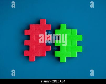 Red and green puzzle blocks between arrows are joining each other on blue background, minimal style. Business partnership, teamwork, collaboration, an Stock Photo