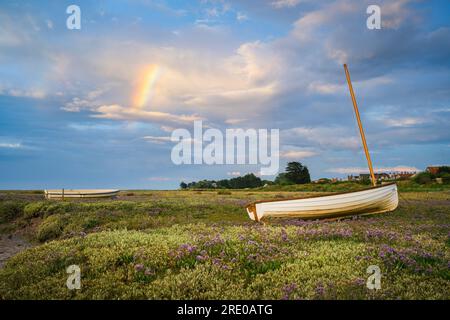 Partial rainbow over the wooden boats on the salt marsh near Brancaster Staithe. Stock Photo