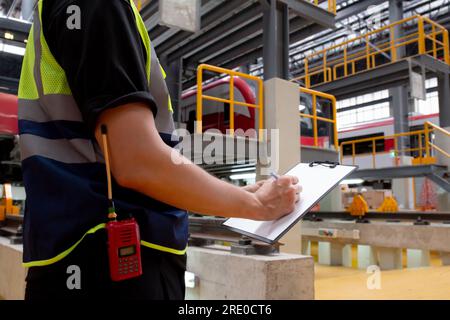 Closeup hands young engineer man or worker checking electric train for planning maintenance and writing document on clipboard in station, transport an Stock Photo
