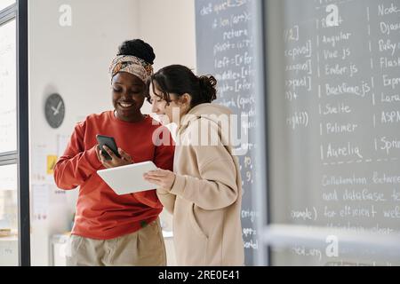 African American teacher showing online presentation on smartphone to student at IT lesson Stock Photo