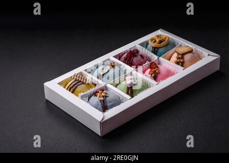 Delicious sweet colorful mochi desserts or ice cream with rice dough and toppings in a cardboard box on a dark concrete background Stock Photo