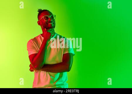 Thoughtful young man with dreadlocks, guy thinking over gradient yellow-green background in neon. Stock Photo