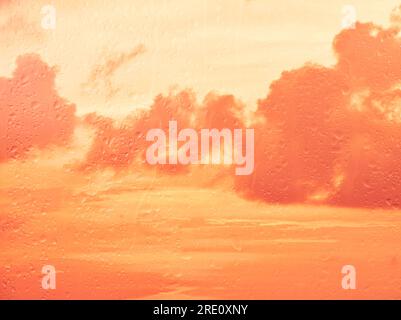 Close up raindrops and water runs on glass window pane surface over vivid orange sunset sky background on rainy day Stock Photo