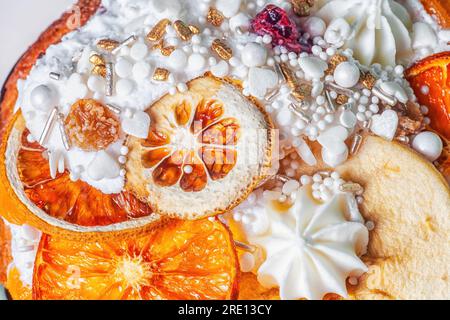 Easter cake decor closeup. Fruitcake decorated dried orange slices, apples, white meringue, icing, candies sprinkled close up. Festive tasty baked kul Stock Photo