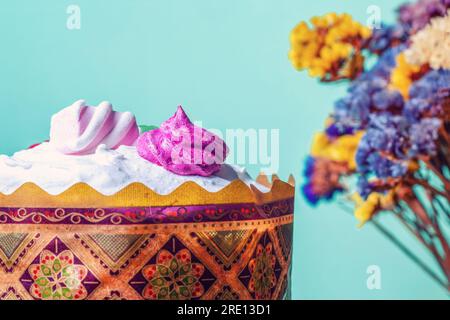 Easter cake, dry Statices flowers on blue background. Bake Kulich decor white ice, marshmallows and Limonium bouquet. Paschal traditional sweet bread Stock Photo