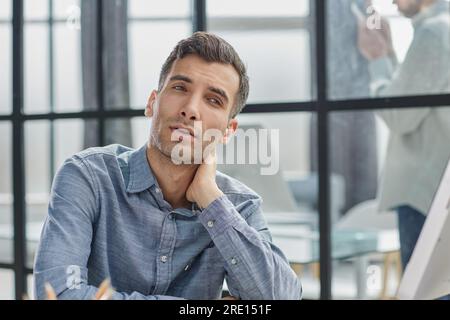 thoughtful male employee thinking over an idea while sitting at a desk in the office Stock Photo