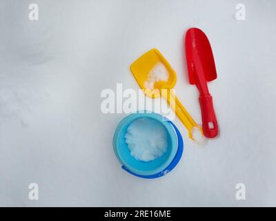 Colorful plastic children toys in white winter snow playground, shovel, trowel, scoop, bucket, high angle view, copy space Stock Photo