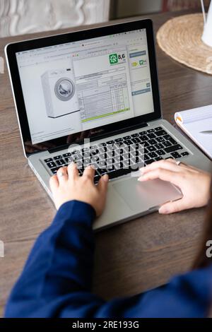 A woman consults the reparability label of a washing machine on a web store store. Manufacturers must indicate on a scale of A E how easily their devi Stock Photo