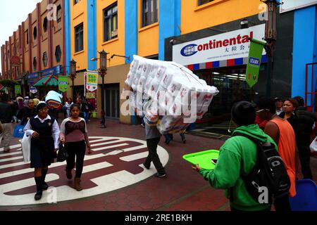 Man carrying bundles of polystyrene trays and toilet rolls through pedestrian street in Chinatown area of central Lima, Peru Stock Photo