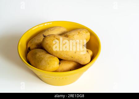 Closeup view of group of fresh ripe mango fruit in bright yellow ceramic bowl isolated on white background Stock Photo