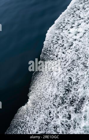 Bow waves of a ship with foam on the water of the blue sea. Aside splashing water and foam Stock Photo