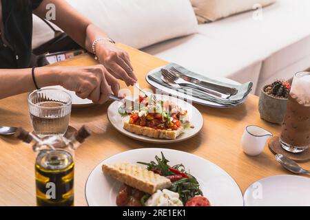 Female hands hold knife and fork cutting bruschetta appitizer on the plate. Stock Photo