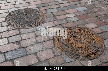 Two decorated manhole covers in a street in the Lithuanian town of Kaunas Stock Photo