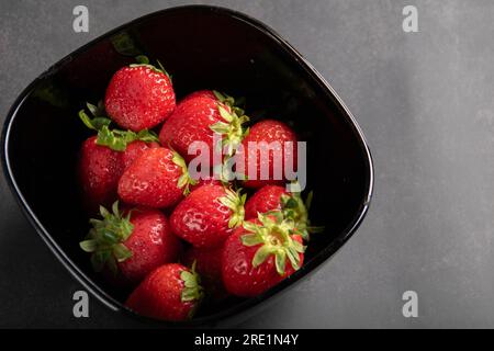 photo of a strawberry lying in a deep black plate on a gray background. Stock Photo