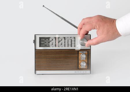 Authentic 70s radio receiver. With a man's hand on the wave-tuning regulator. Isolated on white background. Traces of time and scuffs on the body Stock Photo