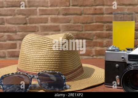 Camera with  sunglasses and brimmed straw hat on wooden table Stock Photo