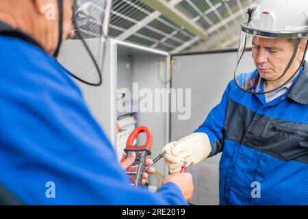 Two Service Engineers or electrician working on checking transformer site and solving problem for green energy solar power plant operation. Technician Stock Photo
