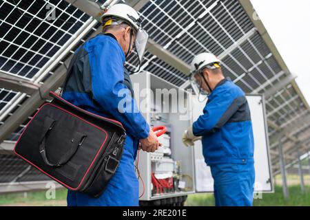 Two Service Engineers or electrician working on checking transformer site and solving problem for green energy solar power plant operation. Technician Stock Photo