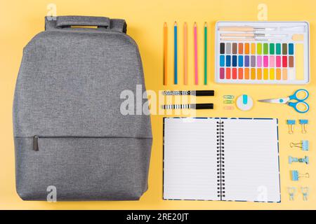 Education, learning, back to school background. Knolling composition with backpack and different school stationery supplies on yellow background. Top Stock Photo