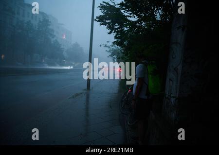 Berlin, Germany. 24th July, 2023. A person tries to protect himself from the rain on the wall. Credit: Annette Riedl/dpa/Alamy Live News Stock Photo