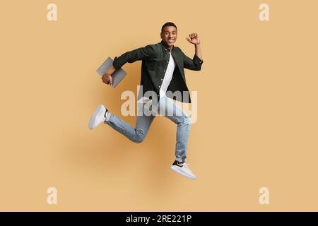 Excited young black guy independent contractor running with computer Stock Photo