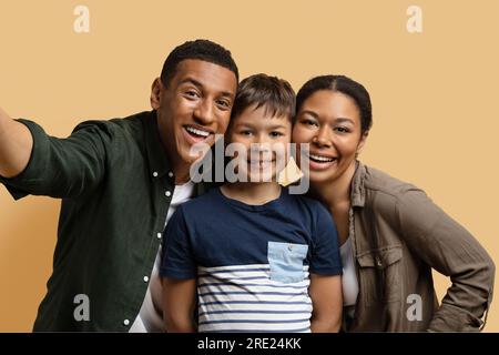 Happy cheerful family taking selfie together on beige Stock Photo