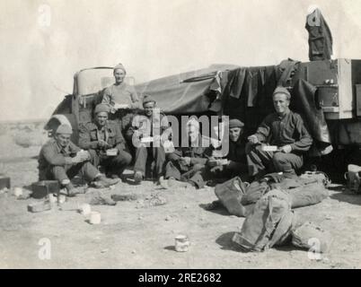 Libya. 1942. British soldiers eating a meal from mess tins whilst sitting in front of a pair of Canadian Military Pattern (CMP) trucks near Msus, Libya in January 1942. The photograph was taken during the North African campaign of the Second World War. Stock Photo