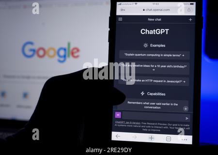 Azores, Portugal - 16.01.2023: Hand hold Mobile Phone with AI ChatGPT home page. Developed by OpenAI. In the background a laptop screen with defocused Stock Photo