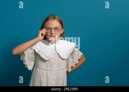 Try on glasses. Vintage portrait of a girl trying on glasses. Retro clothes. Blue background. Copyspace Stock Photo
