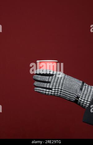 Woman's hand in a glove holds a paper cup for coffee. Red background Stock Photo