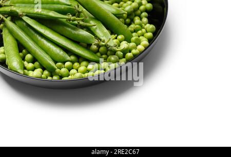 Fresh green peas in pods and peeled green pea seeds in a black round plate, isolated on white background. Vegetable protein, healthy products. Stock Photo