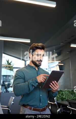 Smiling busy young Latin business man using tablet standing in office. Stock Photo