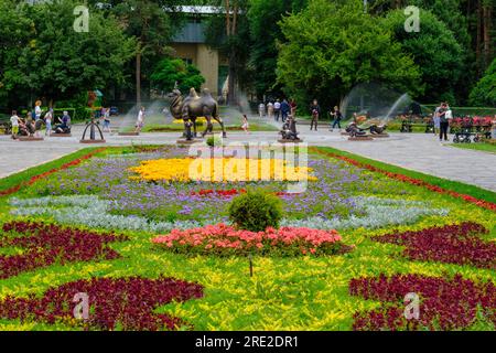 Kazakhstan, Almaty. Flower Bed at Entrance to Central Park for Culture and Recreation. Bactrian Camel Statue and Signs of the Eastern Zodiac in backgr Stock Photo